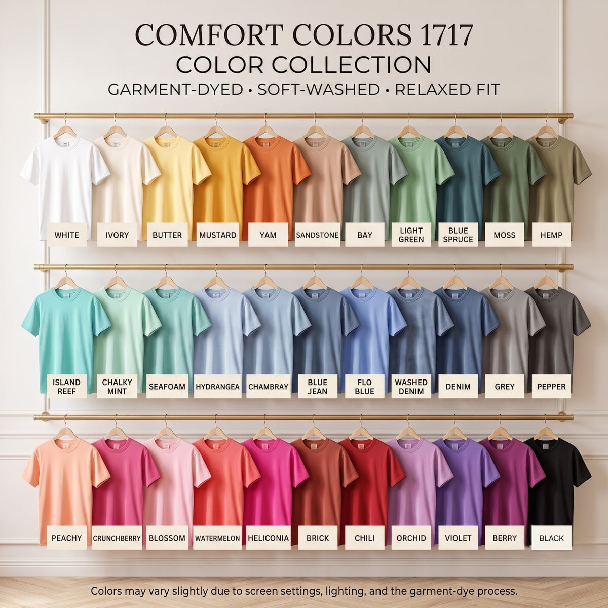 A display for the Comfort Colors 1717 color collection, showing rows of short-sleeve shirts on hangers in many different garment-dyed colors against a light beige wall. Images of shirts with labels include White, Ivory, Butter, Mustard, Yam, Sandstone, Bay, Light Green, Blue, Green, Moss, Hemp, Island Reef, Chalky Mint, Seaf Foam, Hydrangea, Chambray, Blue Jean, Flo Blue, Washed Denim, Denim, Grey, Pepper, Peachy, Crunchberry, Blossom, Watermelon, Helicon, Brick, Chili, Orchid, Violet, Berry, and Black.